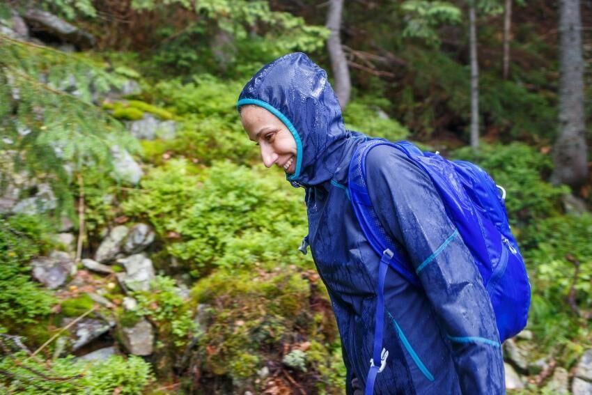 Wer sich häufiger draußen aufhält muss mit wechselndem Wetter rechnen Frau in Regenausrüstung am Waldesrand - Wasserfester Rucksack